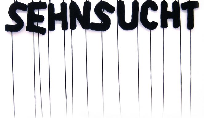 Das Wort "SEHNSUCHT" in fetten schwarzen Buchstaben hängt an Schnüren vor einem weißen Hintergrund.