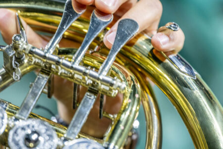 Nahaufnahme einer Hand, die die Ventile eines Waldhorns aus Messing drückt, mit detaillierten Metallarbeiten und den Fingern des Musikers.