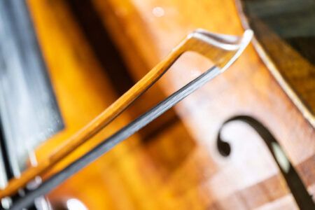 Nahaufnahme eines Cellobogens, der über die Cellosaiten gezogen wird, wobei die hölzerne Oberfläche des Instruments und das F-Loch im Hintergrund zu sehen sind.