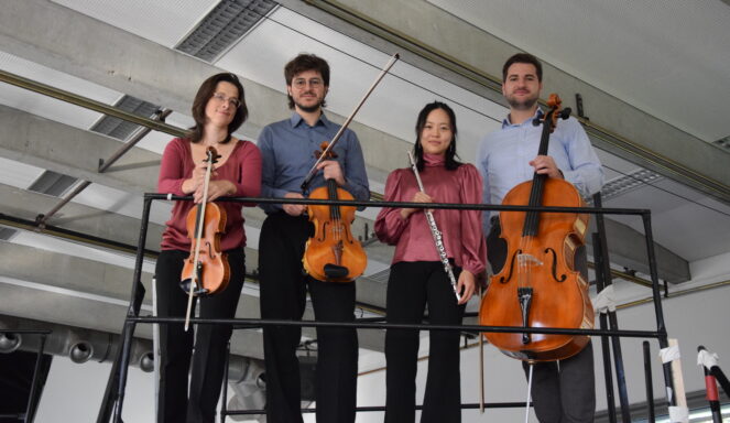 Vier Musiker stehen auf einer Bühne und halten eine Geige, eine Bratsche, eine Flöte und ein Cello in den Händen.